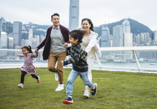 Young Asian parents with two kids happily running in a park with city scape behind them