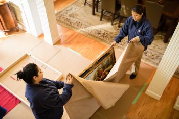 Two Hispanic women pack up painting at clients home