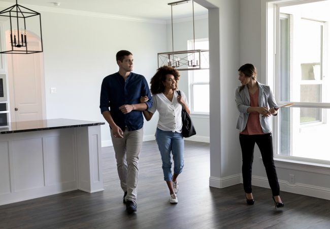 Realtor shows a couple a home. The realtor shows them the home's large living and kitchen area. The couple is expecting their first child.