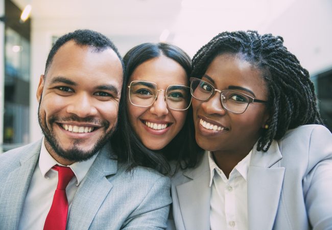 Coworkers, a man and two women pose in business attire at the office