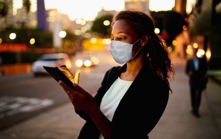 Businesswoman using a digital tablet at night in the city wearing a face mask.