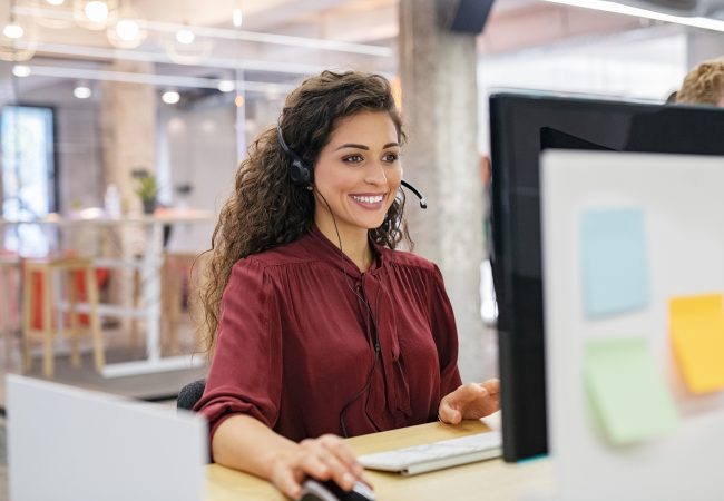 Young woman taking call on headset while on the computer