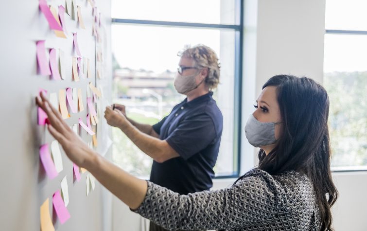 Two people leading a brainstorming session by putting post it notes on the wall