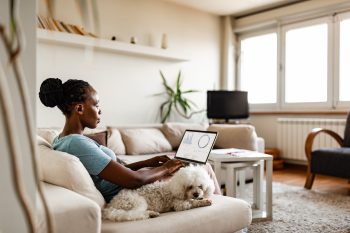 Woman working remotely on her couch with her dog next to her