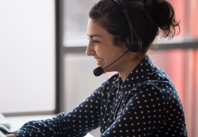 Positive woman worker with earphones helping to solve customer problems close up.