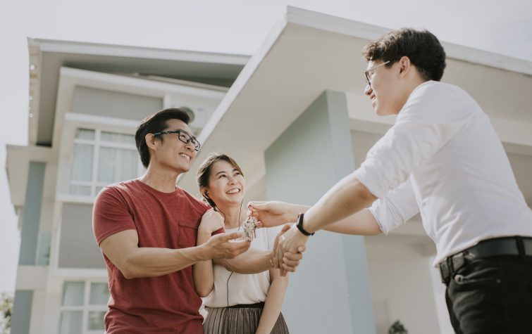 Smiling couple collecting house keys from real estate agent after buying a house