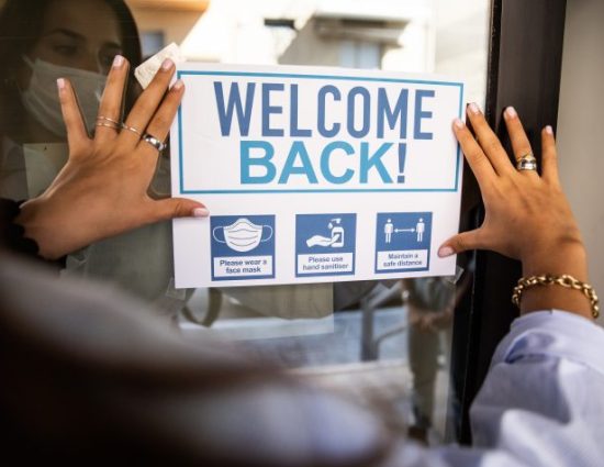 Woman applying "Welcome Back" sign to the building entrance to welcome the employees back.