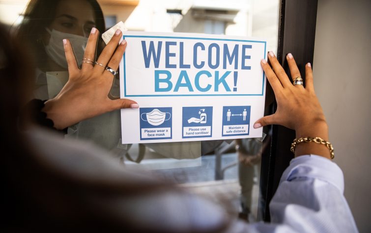 Woman applying "Welcome Back" sign to the building entrance to welcome the employees back.