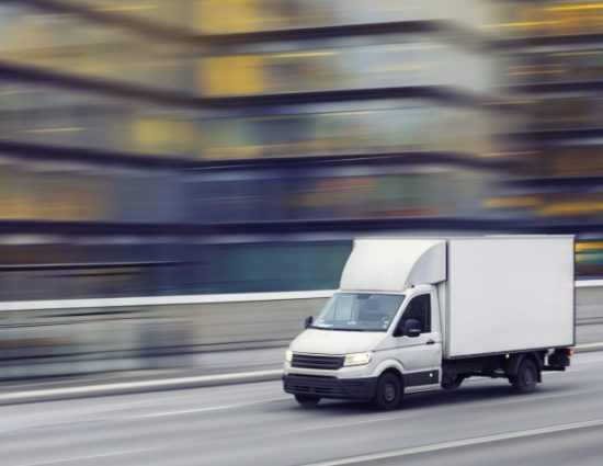 A delivery truck travelling fast on a city street with motion blurred office buildings in the background.