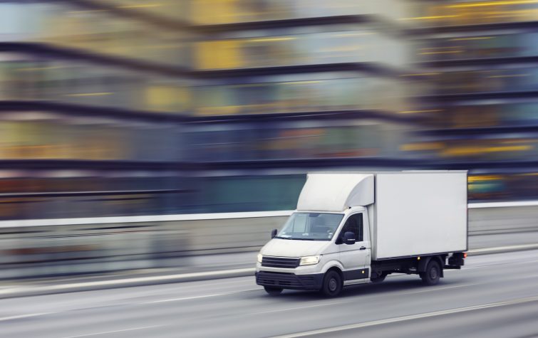 A delivery truck travelling fast on a city street with motion blurred office buildings in the background.