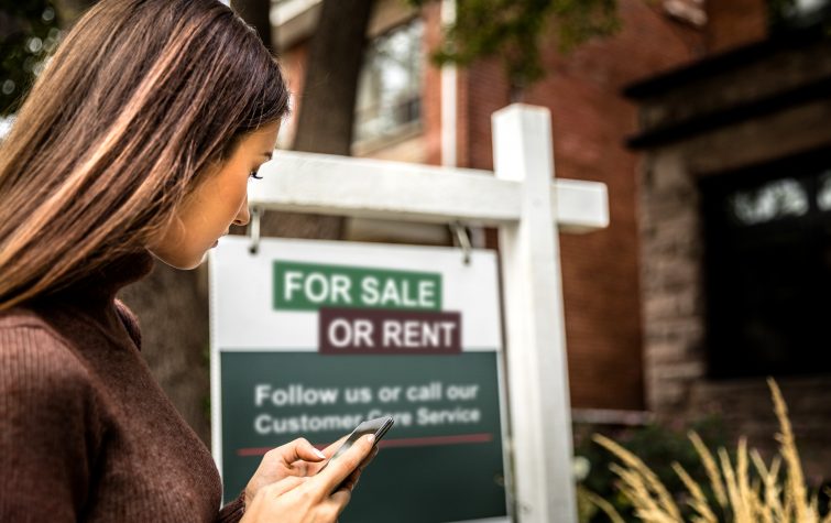 Woman standing in front of for sale or rent sign