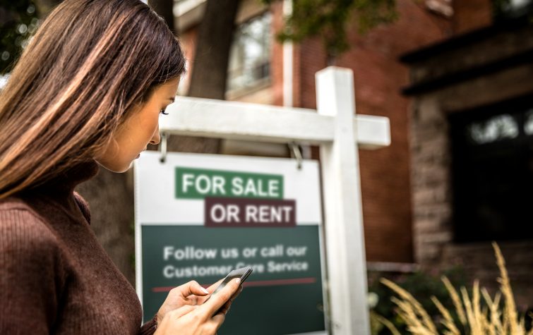 Woman standing in front of for sale or rent sign