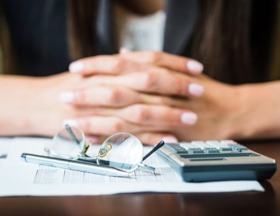 Close up of businesswoman's hands with pen, glasses, and calculator doing some financial calculations