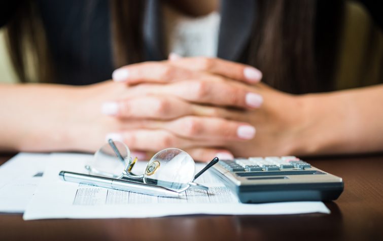 Close up of businesswoman's hands with pen, glasses, and calculator doing some financial calculations