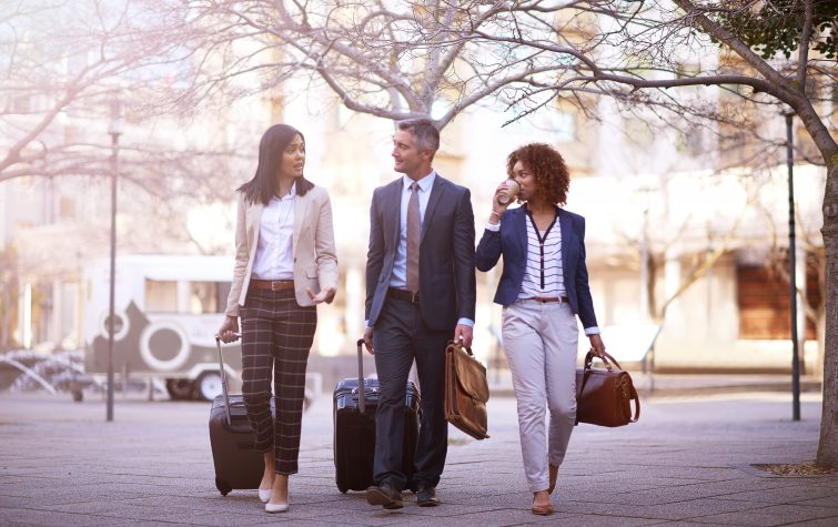 3 business people walking and talking to each other while carrying their luggage outside