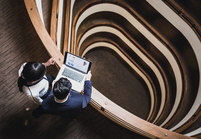 Aerial view of a man and woman looking at a laptop screen positioned on a railing