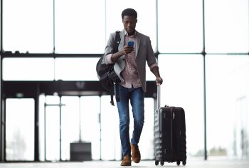 Young mobile traveler walking through the airport while looking at his phone