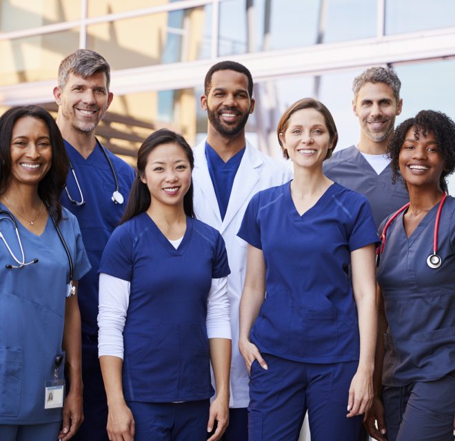 Group of eight men and women dressed in medical attire smiling