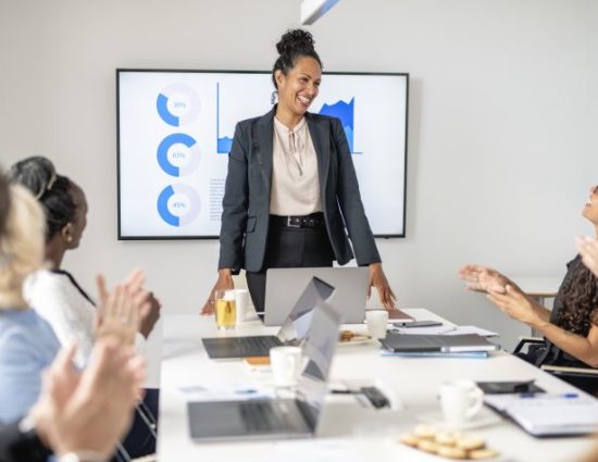 Personal perspective of business professional in early 40s smiling as colleagues applaud successful presentation in office board room.