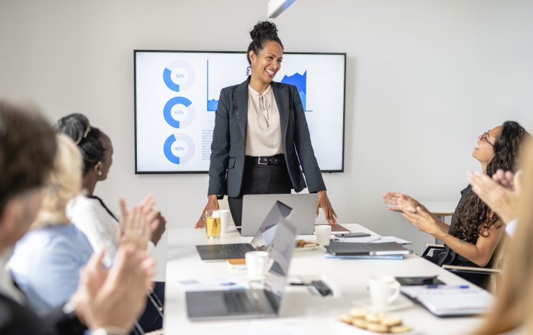 Personal perspective of business professional in early 40s smiling as colleagues applaud successful presentation in office board room.