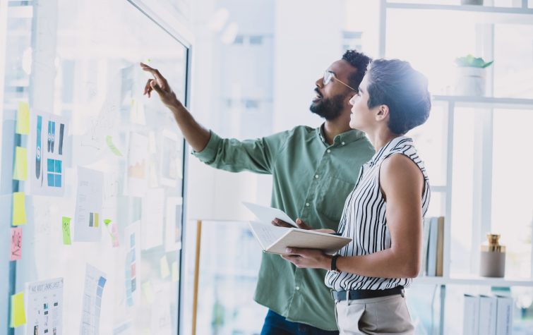 Shot of two businesspeople brainstorming with notes on a glass wall in an office