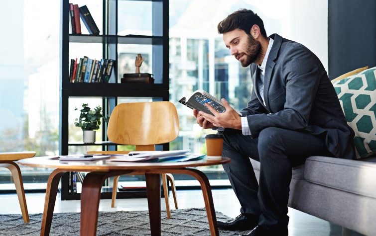 Shot of a young businessman reading a book in a modern office