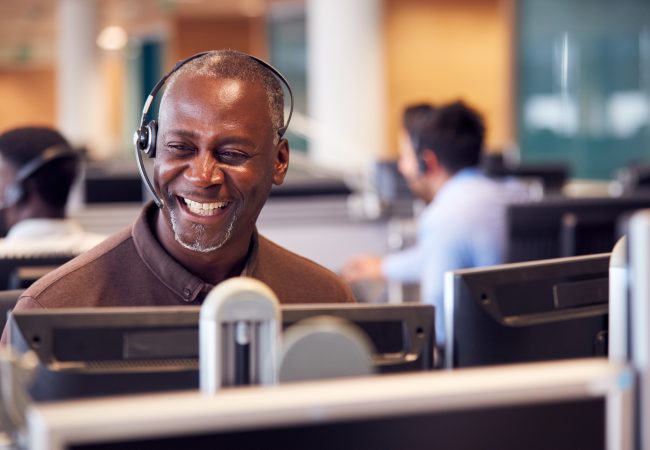 Man with headset smiling in front of a computer