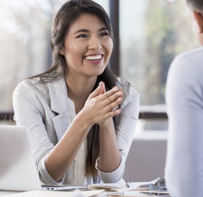 Young asian woman sitting across table talking to coworker