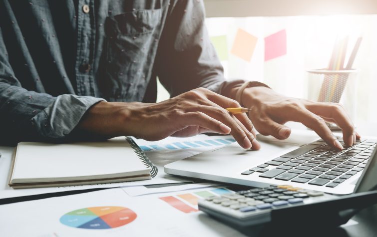 Close up of businessman or accountant hand holding pen working on laptop computer for calculate business data, accountancy document and calculator at office