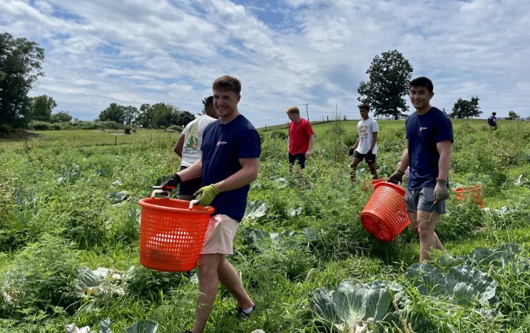 two farm workers smiling while carrying baskets in a field