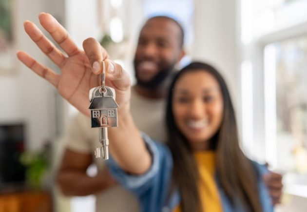 Happy couple holding house keys outside their new forever home, representing the shift away from starter homes in today's housing market