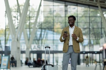 Professional traveler with suitcase checking smartphone at airport during international relocation