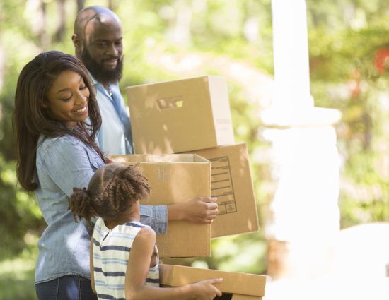 Family carrying boxes into their new home during a summer relocation move