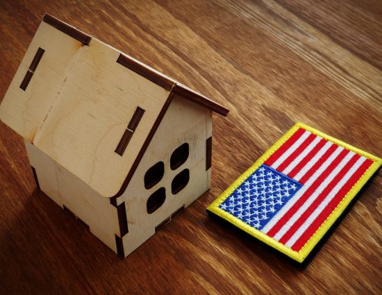 Wooden model home beside a U.S. flag representing federal housing law and relocation risks