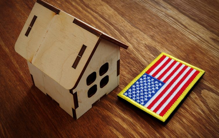 Wooden model home beside a U.S. flag representing federal housing law and relocation risks