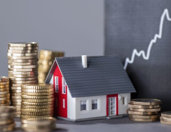 Model house surrounded by stacks of coins with a rising price chart illustrating housing affordability