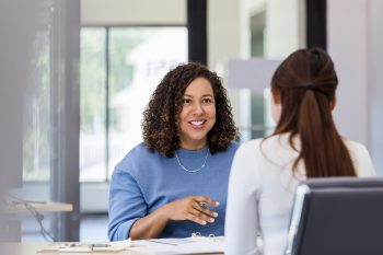 Two female colleagues in a one-on-one office meeting representing the six-month assignee wellbeing check-in that improves international assignment outcomes