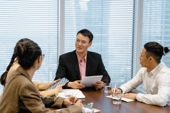 Three HR professionals in a conference room reviewing global mobility cost benchmarks and program strategy with documents and a tablet