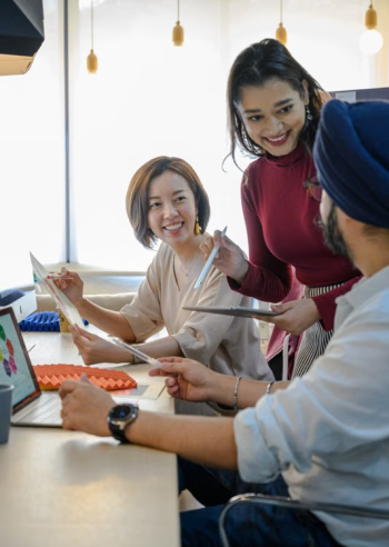 Three diverse colleagues smiling and reviewing documents together in a bright modern office representing the collaborative decision to outsource global mobility
