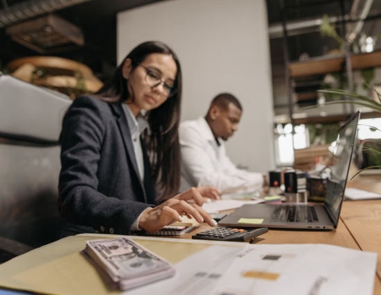 Business professional using a calculator with documents and cash on desk representing relocation cost estimate variance analysis in a mobility program