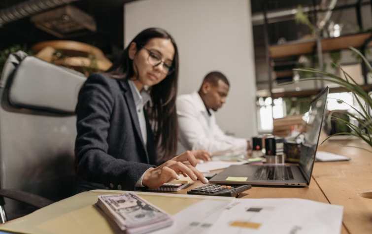 Business professional using a calculator with documents and cash on desk representing relocation cost estimate variance analysis in a mobility program