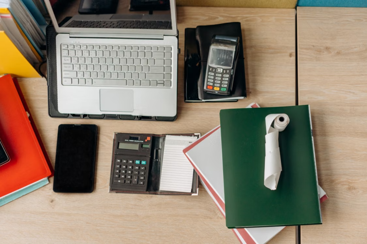 Overhead view of a desk with laptop, calculator, binders, and receipt roll representing relocation expense management and cost tracking tools