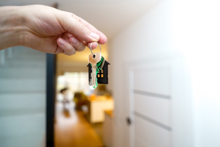 Hand holding house keys with a house keychain in an apartment doorway representing the moment a relocating employee transitions from temporary housing to a permanent home